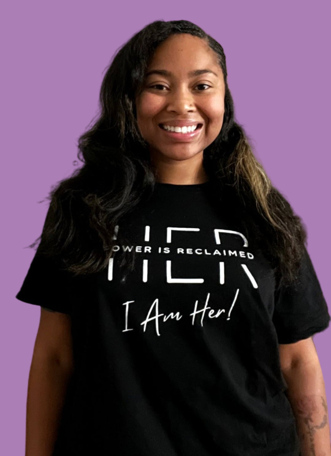 Person wearing a black t-shirt with 'I Am Her!' text on a pink background